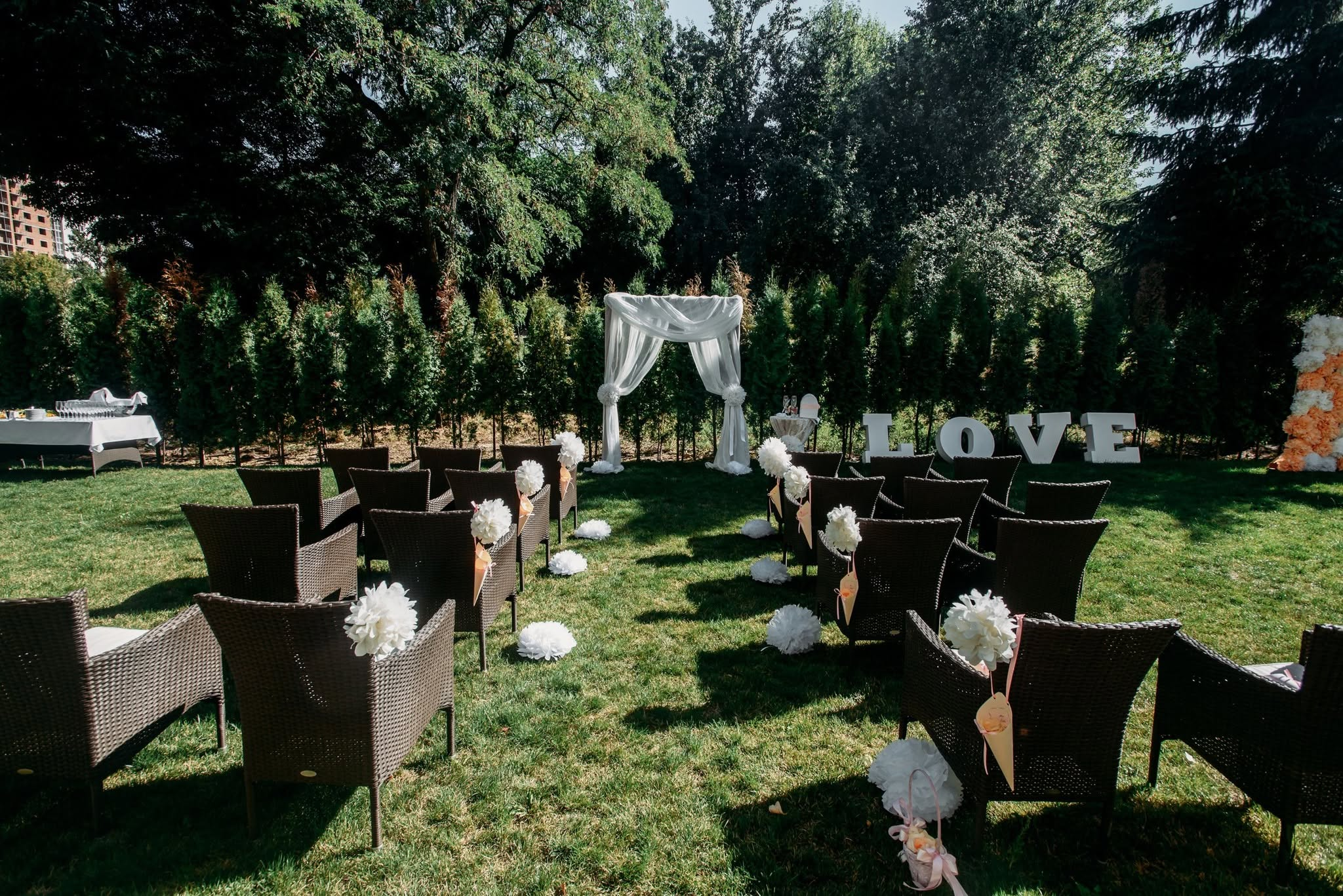 Outdoor wedding lounge on a lawn with wicker seating, white florals and a LOVE letter display