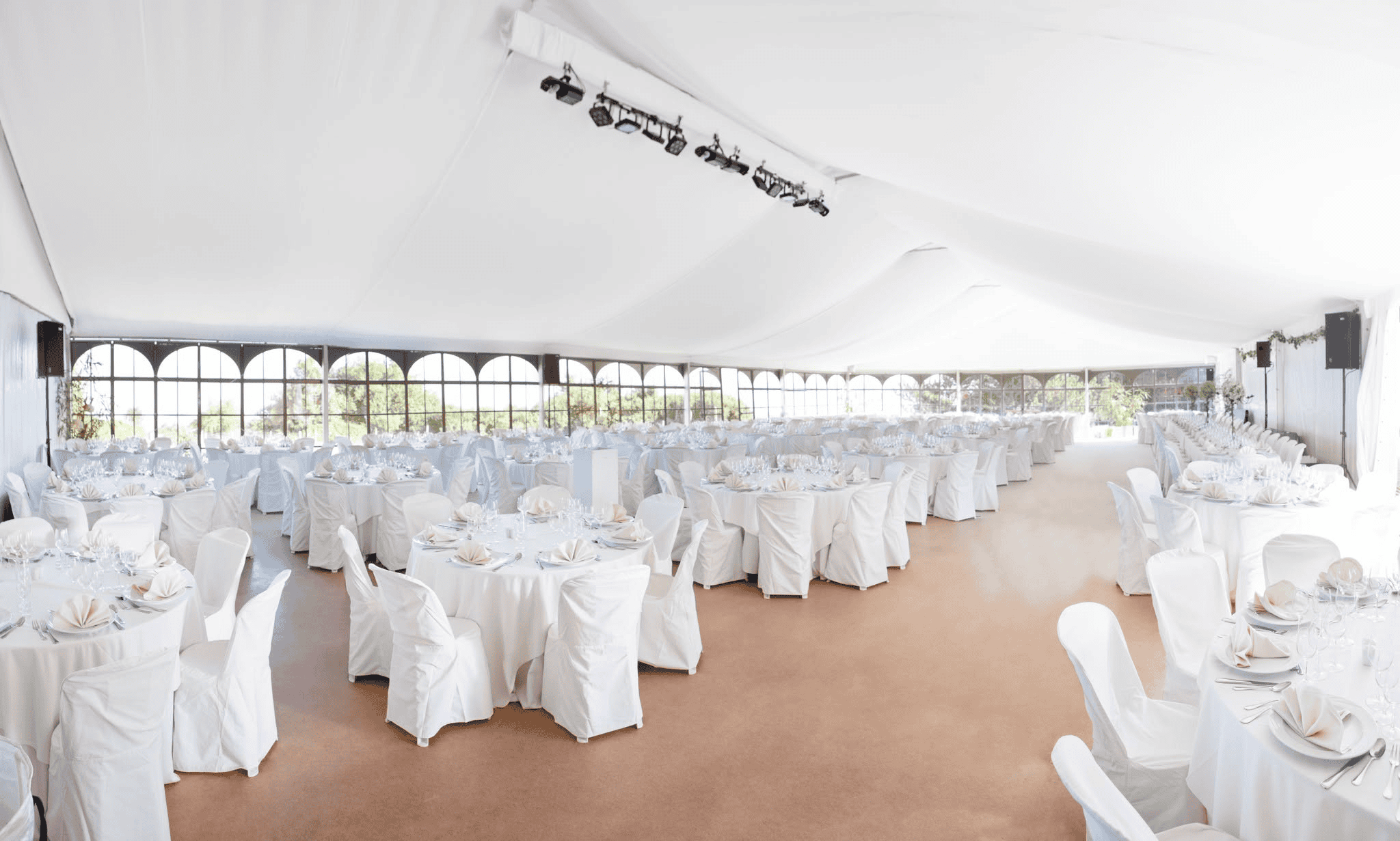Round tables in white chair covers set for a wedding reception inside a structure tent