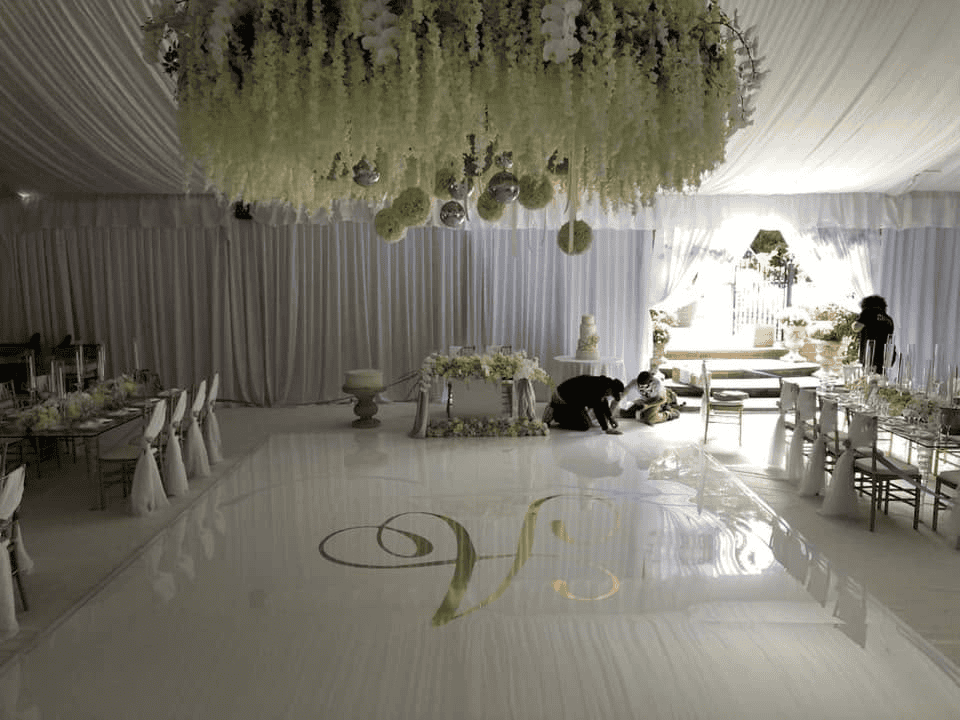 White draped tent with florals hung overhead above a monogrammed dance floor