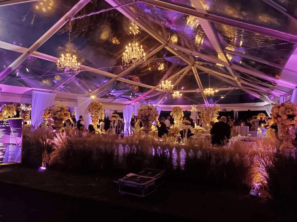 Clear top tent lit in purple at night with chandeliers and tall centerpieces