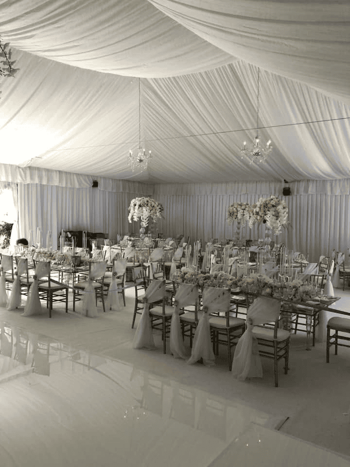 Long tables and gold chairs under a white draped tent ceiling with chandeliers