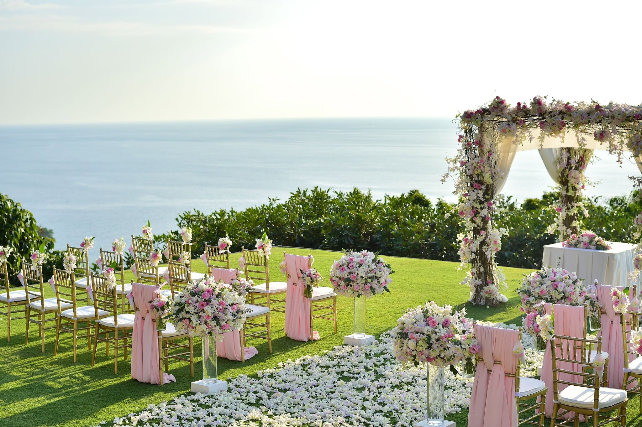 Wedding ceremony set above the water with a floral arch, gold chairs and blush aisle florals