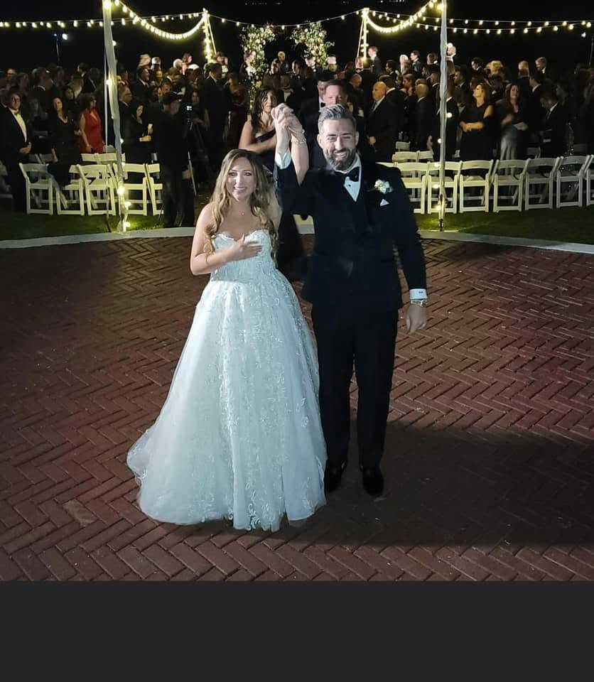 Bride and groom dancing under string lights with guests gathered around the floor