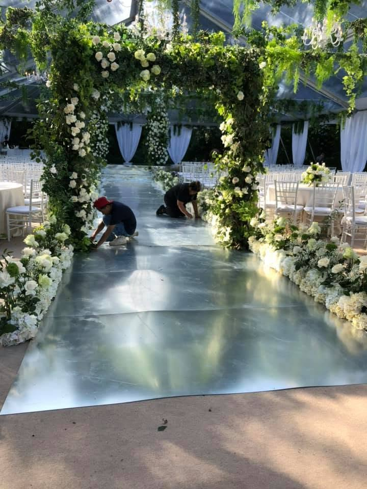 Greenery and floral ceremony arch standing over a mirrored aisle runner