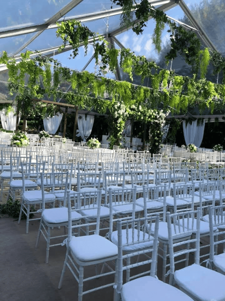 Rows of white chairs under a clear top tent hung with trailing greenery