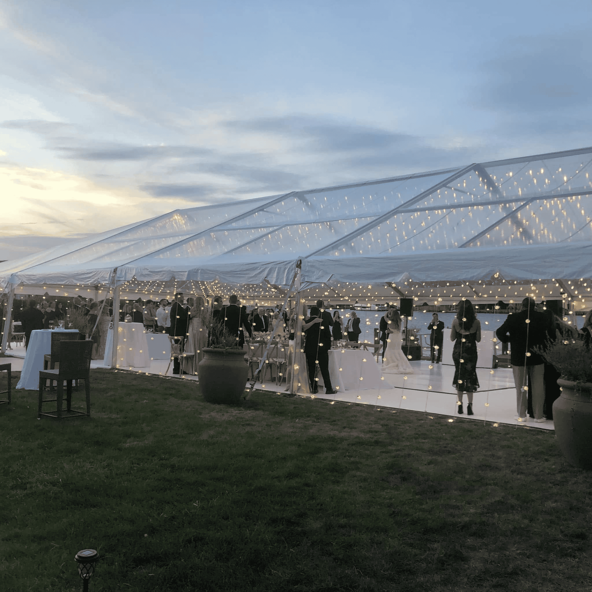 Guests at cocktail hour under a clearspan tent with a transparent roof at dusk
