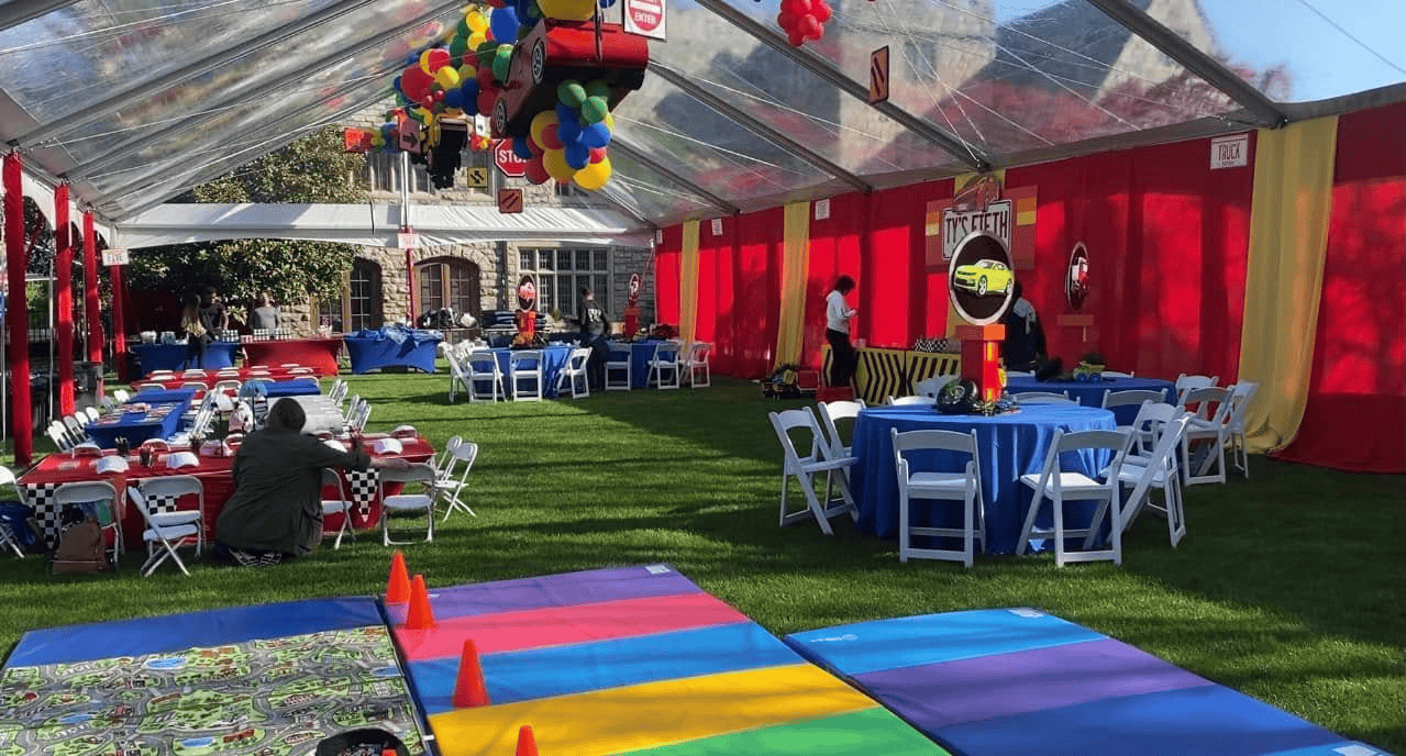 Backyard party under a clear top tent with a red draped wall, a balloon arch and blue linens