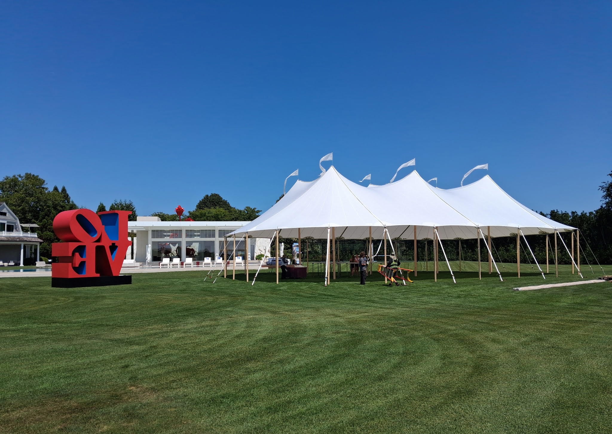Sailcloth tent with wooden center poles lit at dusk over a lawn set for a wedding reception