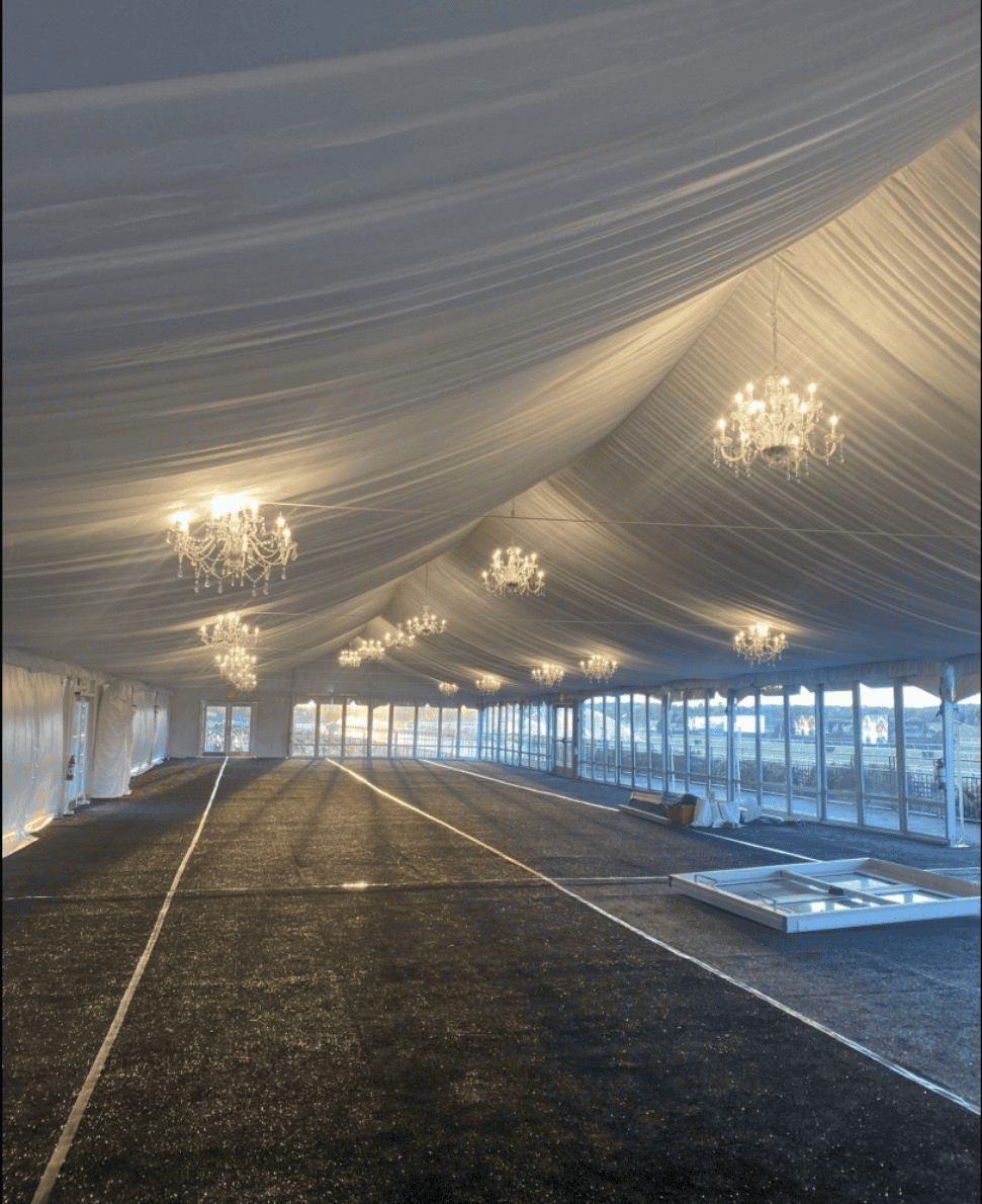 Inside a structure tent looking down its length, ceiling draped and chandeliers hung