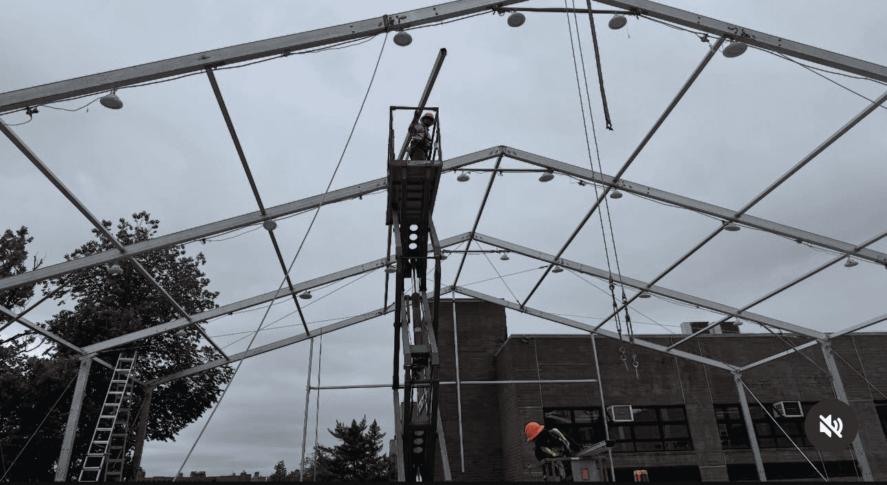 A clearspan tent frame going up, with a crew member working from a lift